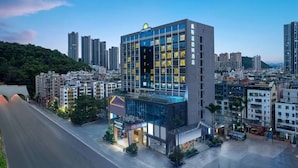 A modern hotel with a glass facade, surrounded by high-rise buildings and a green hill in the background. - Days Hotel BY Wyndham Shenzhen Sanlian (Shenzhen)