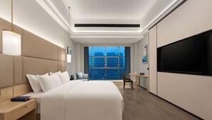 A modern hotel room with a large bed, a desk, a chair, a TV, and a view of the cityscape through the window. - Days Hotel BY Wyndham Shenzhen Sanlian (Shenzhen)