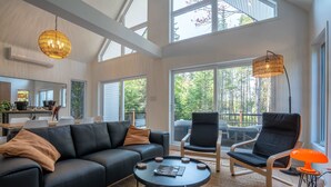 Een ruime woonkamer met een zwarte leren bank, twee zwarte fauteuils, een ronde salontafel en een groot raam met uitzicht op de omgeving.