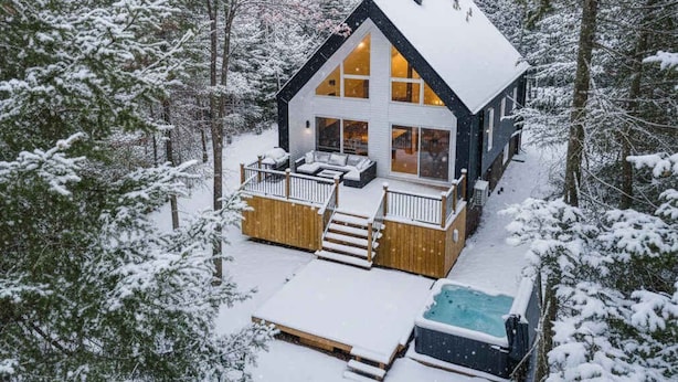Een moderne chalet met een ruim terras, een bubbelbad en uitzicht op een besneeuwd bos.