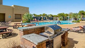 An outdoor pool area with lounge chairs, a barbecue grill, and a building in the background.