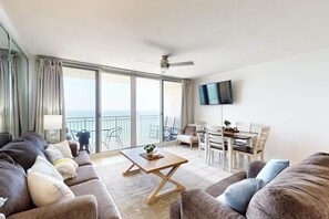 Un vaste salon doté d’une grande porte-fenêtre coulissante donnant sur un balcon, d’un téléviseur à écran plat fixé au mur et d’un coin repas avec une table et des chaises.
