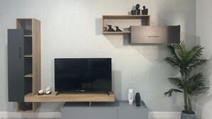 Una sala de estar moderna con un televisor de pantalla plana sobre un soporte de madera, un mueble gris en la parte inferior y un estante montado en la pared con objetos decorativos.