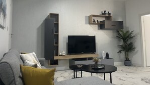 Una sala de estar moderna con un sofá gris, una mesa de centro, un televisor montado en un estante de madera y una planta en maceta.