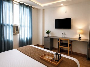 Habitación de hotel con cama, escritorio con televisor, planta y bandeja con vasos y tetera.