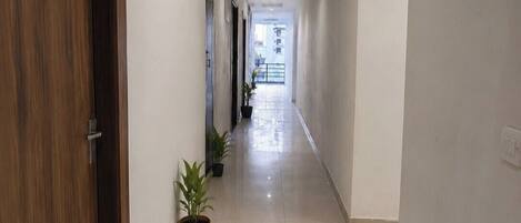 Un couloir avec une porte en bois portant l’inscription « 01 », des plantes en pot et un sol carrelé.