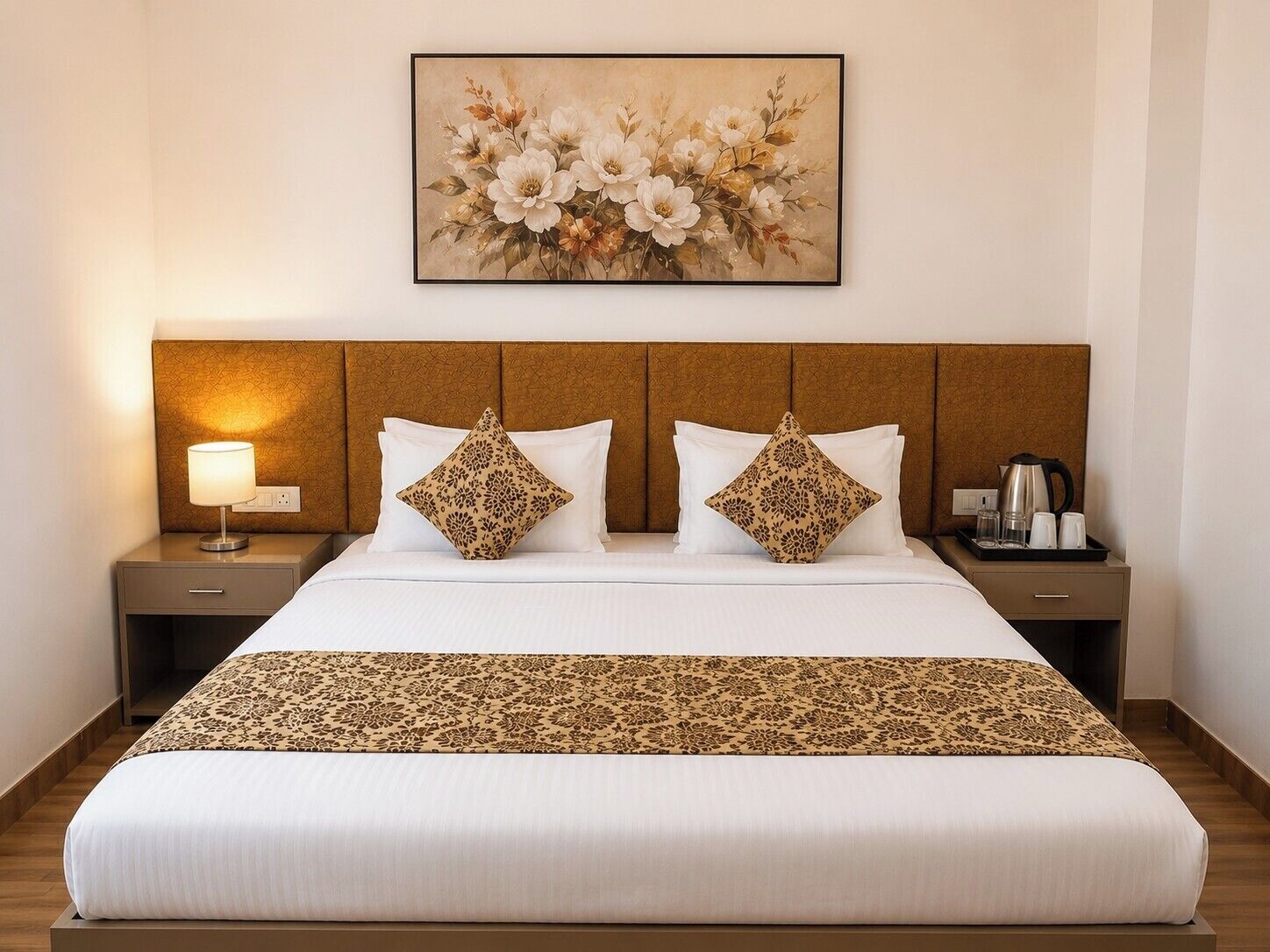 A hotel room with a large bed, two nightstands, a lamp, a coffee maker, and a floral painting on the wall.