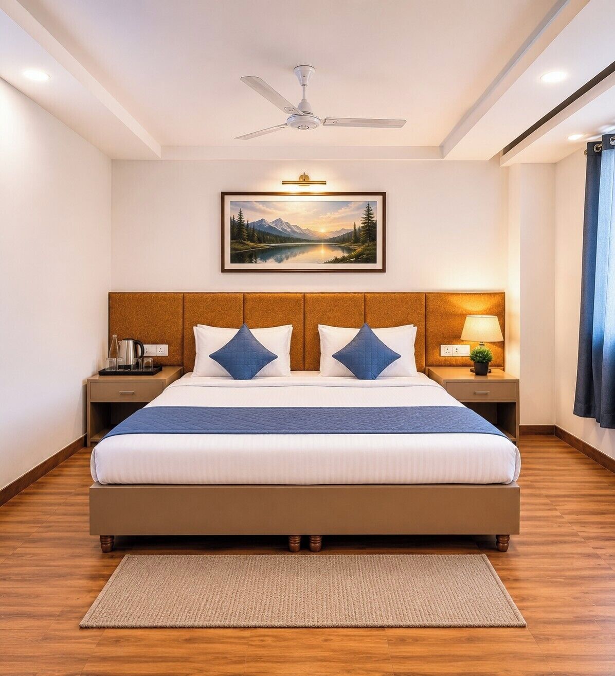 A hotel room with a bed, a ceiling fan, a nightstand with a lamp, a painting on the wall, and a window with curtains.