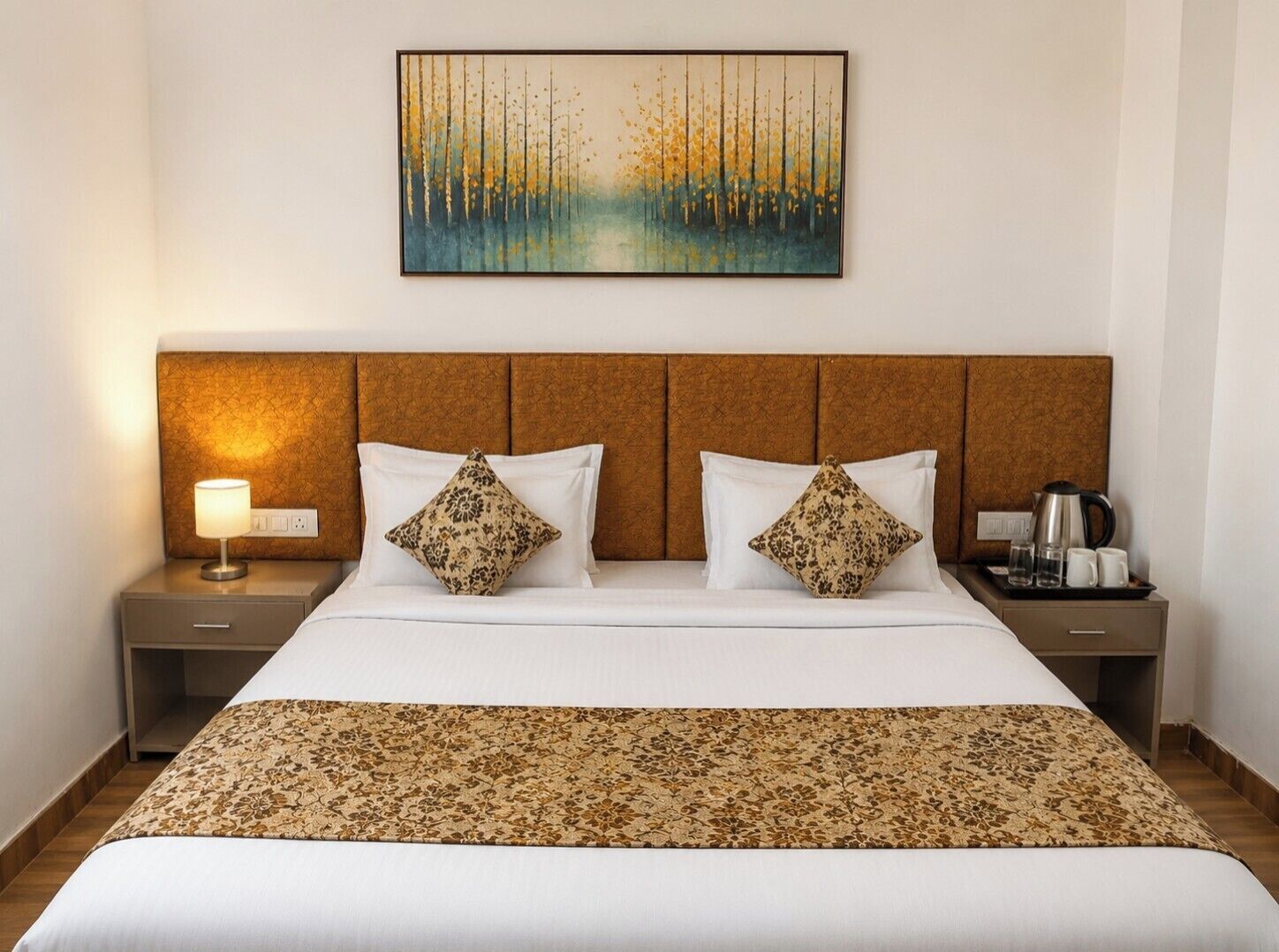 A hotel room with a bed, two nightstands, a lamp, a coffee maker, and a painting on the wall.