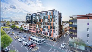 En byggnad med flera våningar och en modern arkitektonisk design, med stora fönster och en kombination av glas- och massiva paneler.