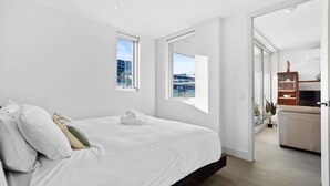 Ett modernt hotellrum med en stor säng, två fönster, utsikt över staden och en sittgrupp med en soffa och ett bord.