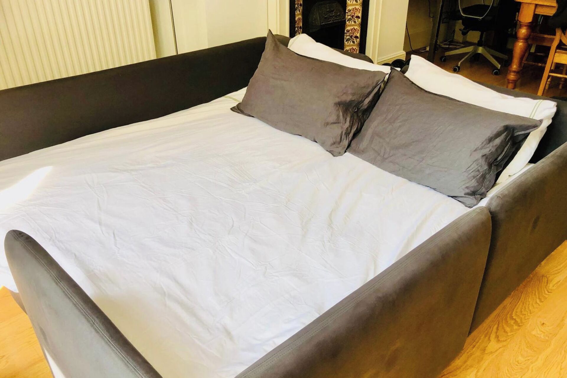 A bed with a white sheet and two pillows, a wooden headboard, and a chair in the background.
