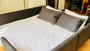 A bed with a white sheet and two pillows, a wooden headboard, and a chair in the background. - 1 Bedroom Flat Sleeps 4 -free Onsite Parking -wifi (London)