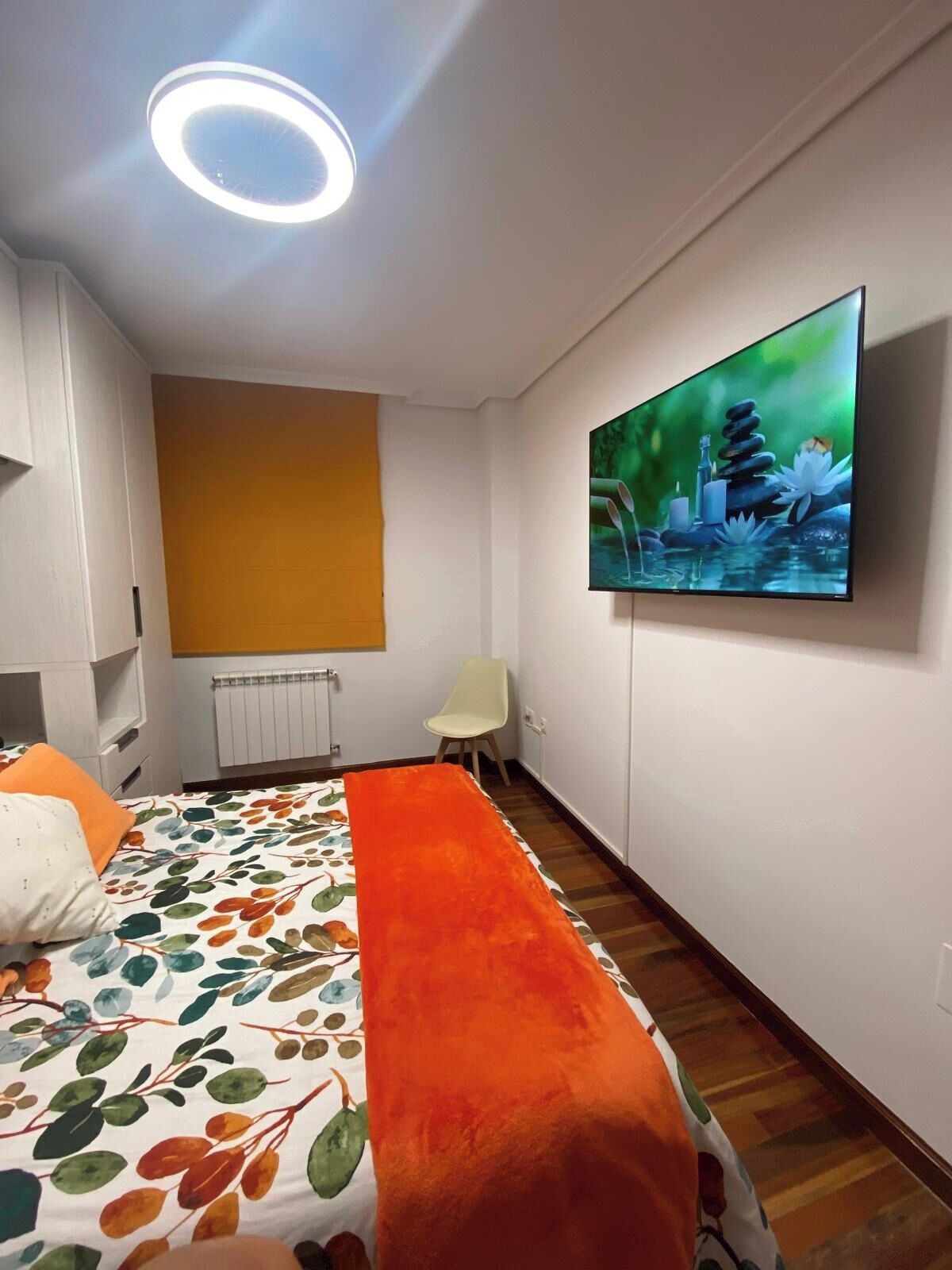 A hotel room with a bed, a TV on the wall, a chair, and a radiator.