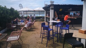 Ein Sitzbereich im Freien mit Tischen und Stühlen, eine Bar und Meerblick.