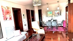 Ein Wohnzimmer mit einer Couch, einem Couchtisch mit Blumen, einem Essbereich mit Stühlen und einem Tisch sowie einer Kristallleuchtre.