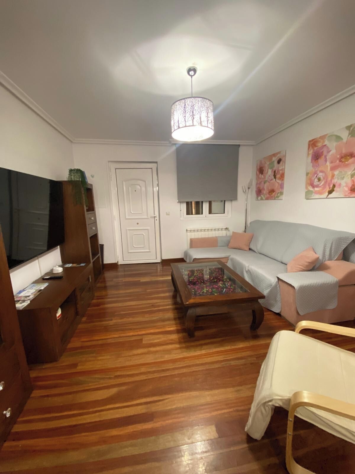 A living room with a wooden floor, a television, a sofa, a coffee table, and a ceiling light.