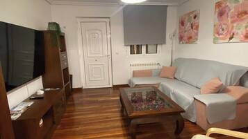 A living room with a wooden floor, a television, a sofa, a coffee table, and a ceiling light.