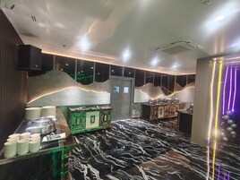 Um interior moderno com piso de mármore, área de buffet com pratos e tigelas, e parede decorativa com design ondulado.