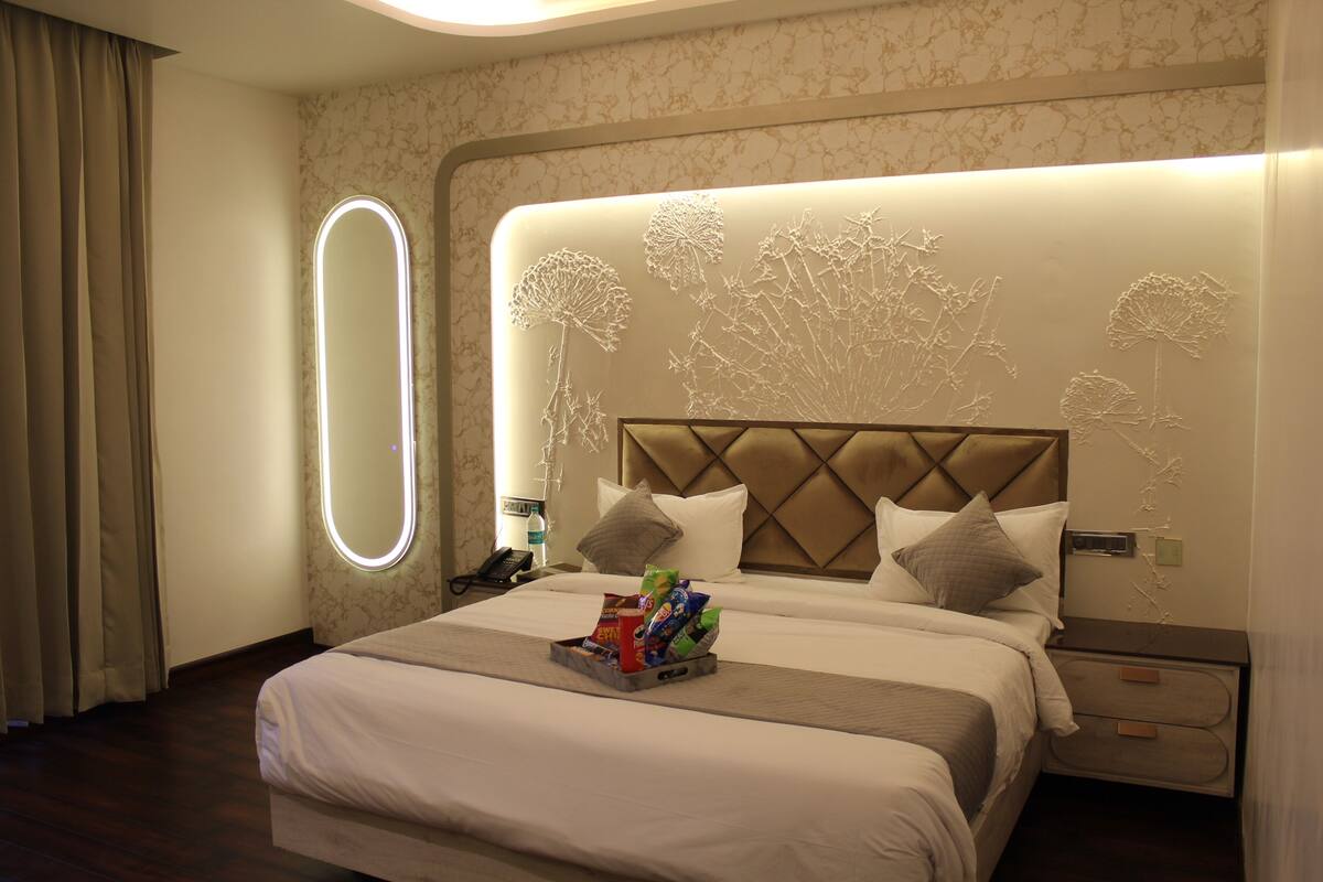 Habitación de hotel con una cama grande, una mesita de noche, un espejo montado en la pared y un panel decorativo.
