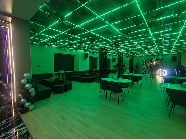 Une pièce avec un plafond éclairé par des néons verts, des canapés noirs et des tables.