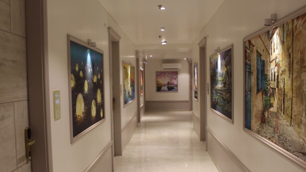 Un pasillo con obras de arte en las paredes, piso de baldosas e iluminación empotrada en el techo.