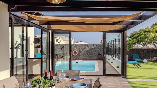 Un espace extérieur aménagé pour les repas, avec vue sur une piscine, un mur en pierre et une pelouse verdoyante.