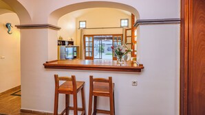 Une cuisine avec deux chaises en bois, un plan de travail en bois et une vue sur l’extérieur grâce à une porte vitrée.