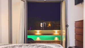 Une chambre avec un lit, une vue sur une piscine la nuit, et une porte donnant sur un espace extérieur.