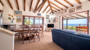 A dining area with wooden chairs and a table, a blue sofa, and a TV. - Villa 'Patrizia' with Sea View, Wi-Fi and Air Conditioning (Castelsardo)