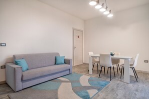 Moderni olohuone, jossa on sohva, ruokapöytä tuoleineen ja kuviollinen matto.