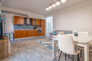 Una cucina moderna con mobili in legno, un forno a microonde e un piano cottura. C'è un'area pranzo con un tavolo e sedie bianche.
