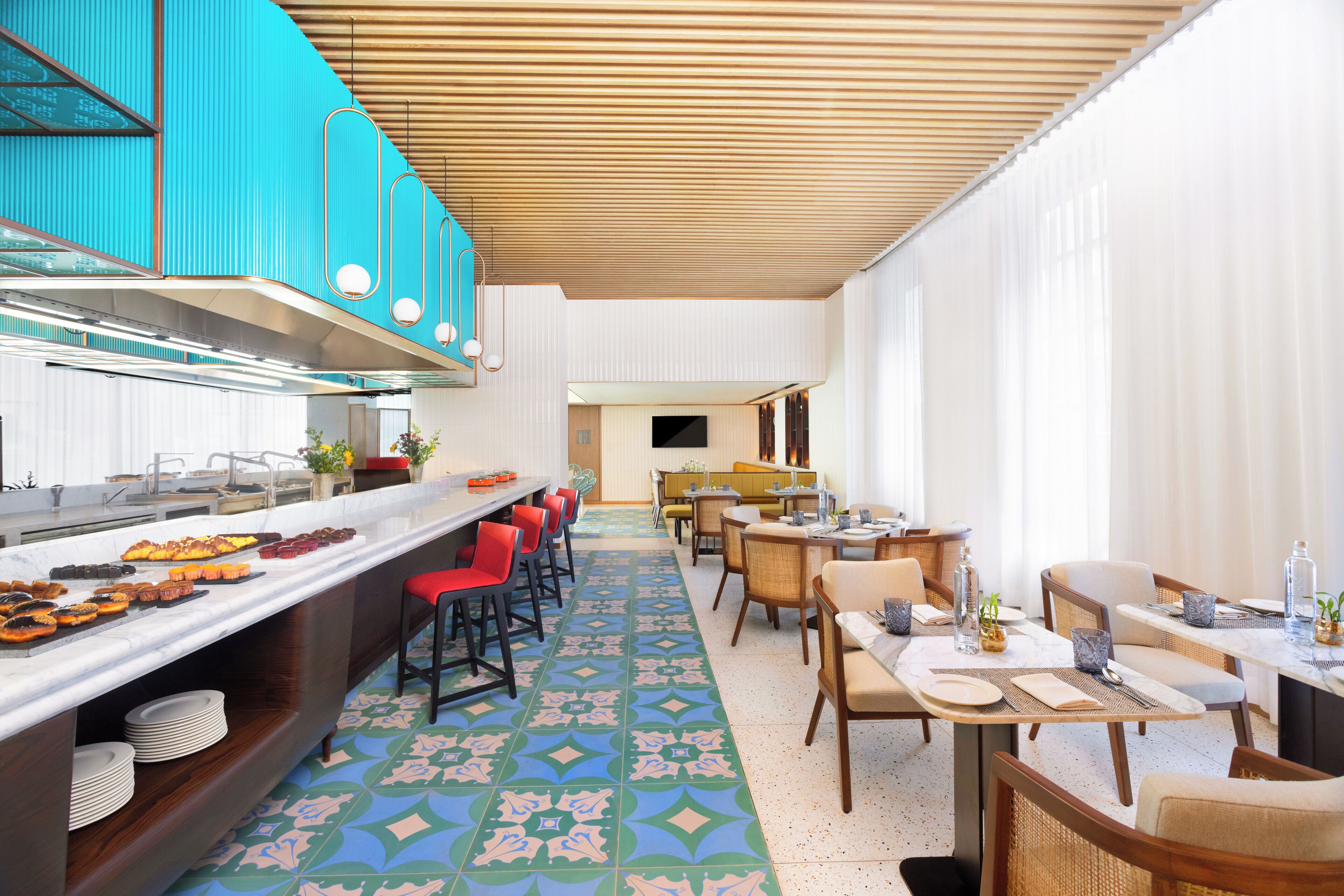 Un área de comedor de hotel moderna con una barra larga, taburetes rojos y un suelo con estampado.