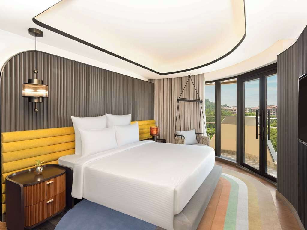 A modern hotel room with a large bed, a hanging chair, and a balcony with a city view.