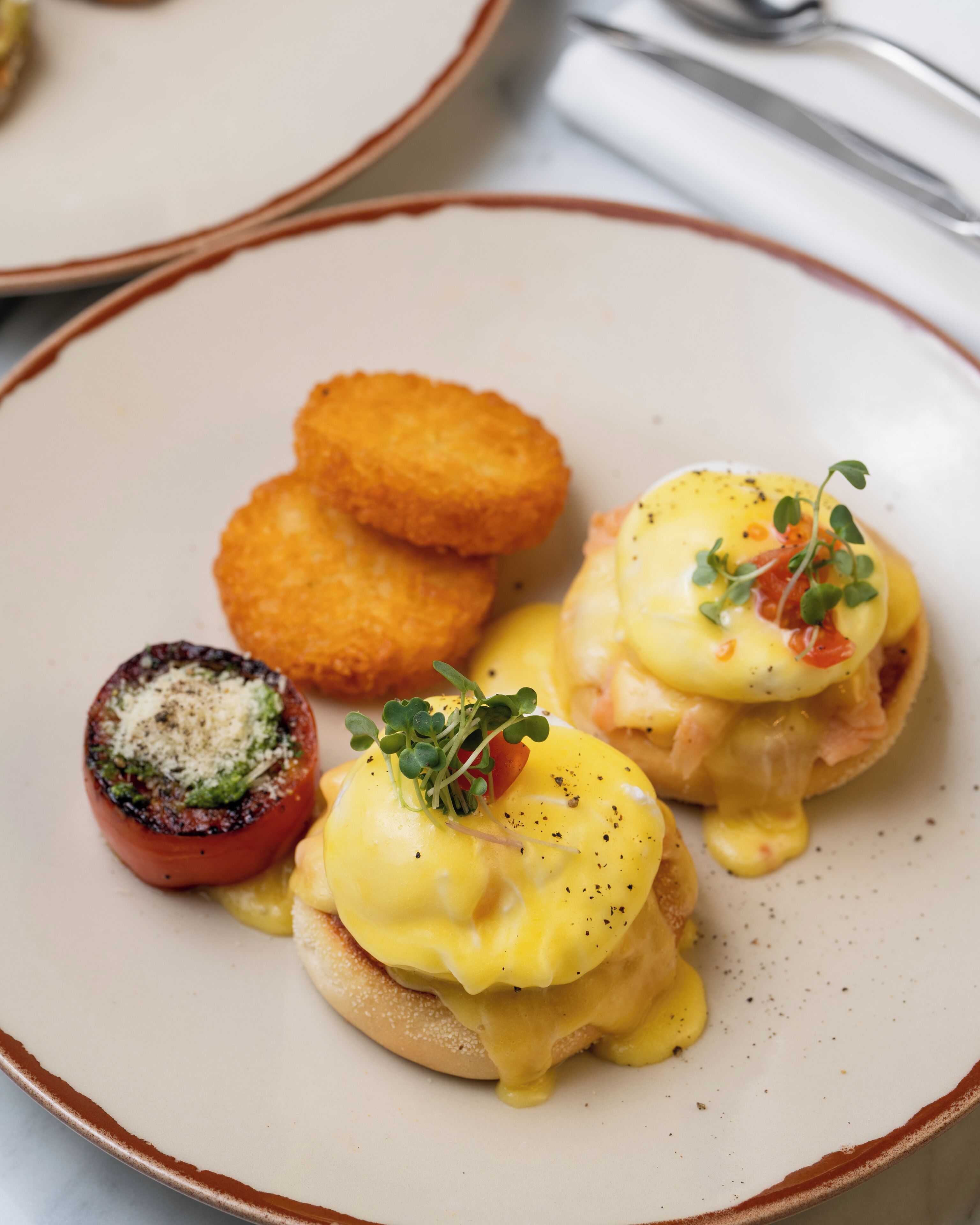 En tallrik med ägg benedict, en grillad tomat och friterade rätter.