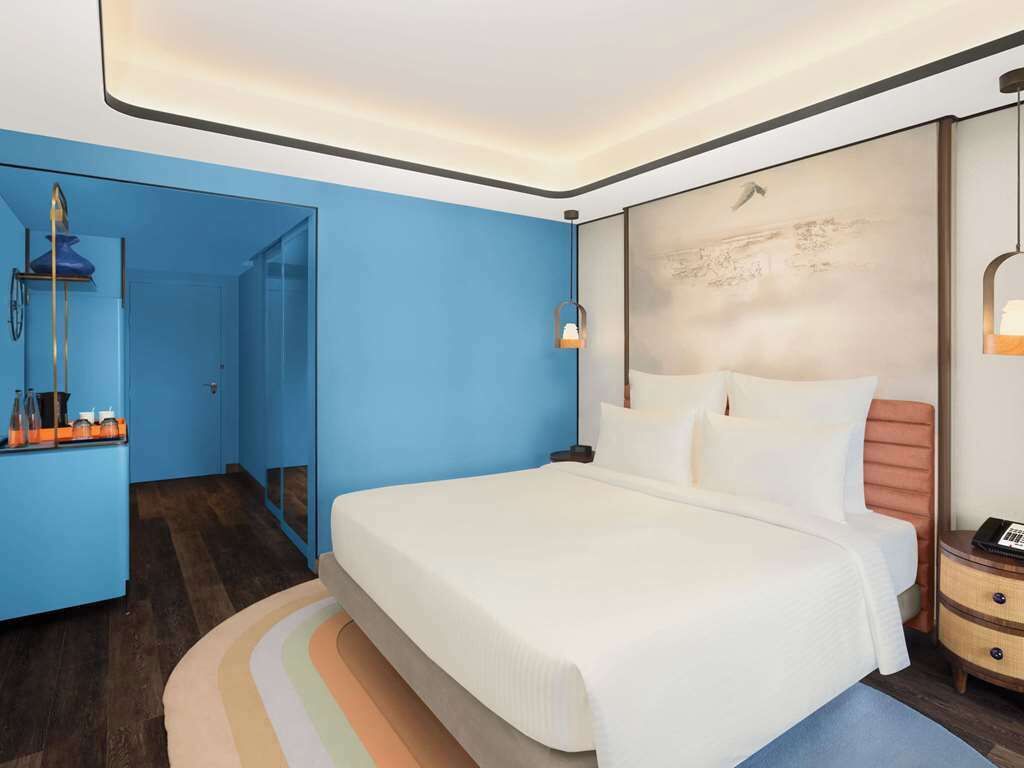 Habitación de hotel moderna con una cama grande, una mesita de noche y un baño visible a través de una puerta abierta.