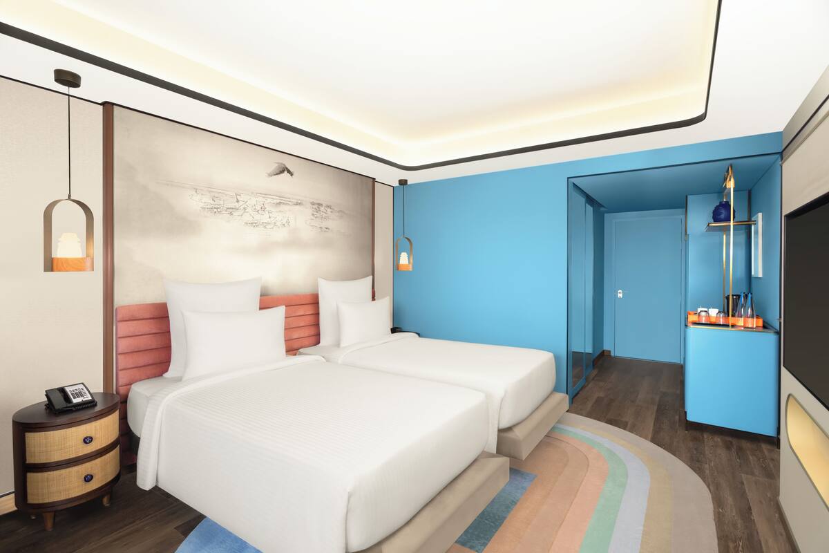 A modern hotel room with two beds, a nightstand with a phone, a wall-mounted artwork, and a blue accent wall.