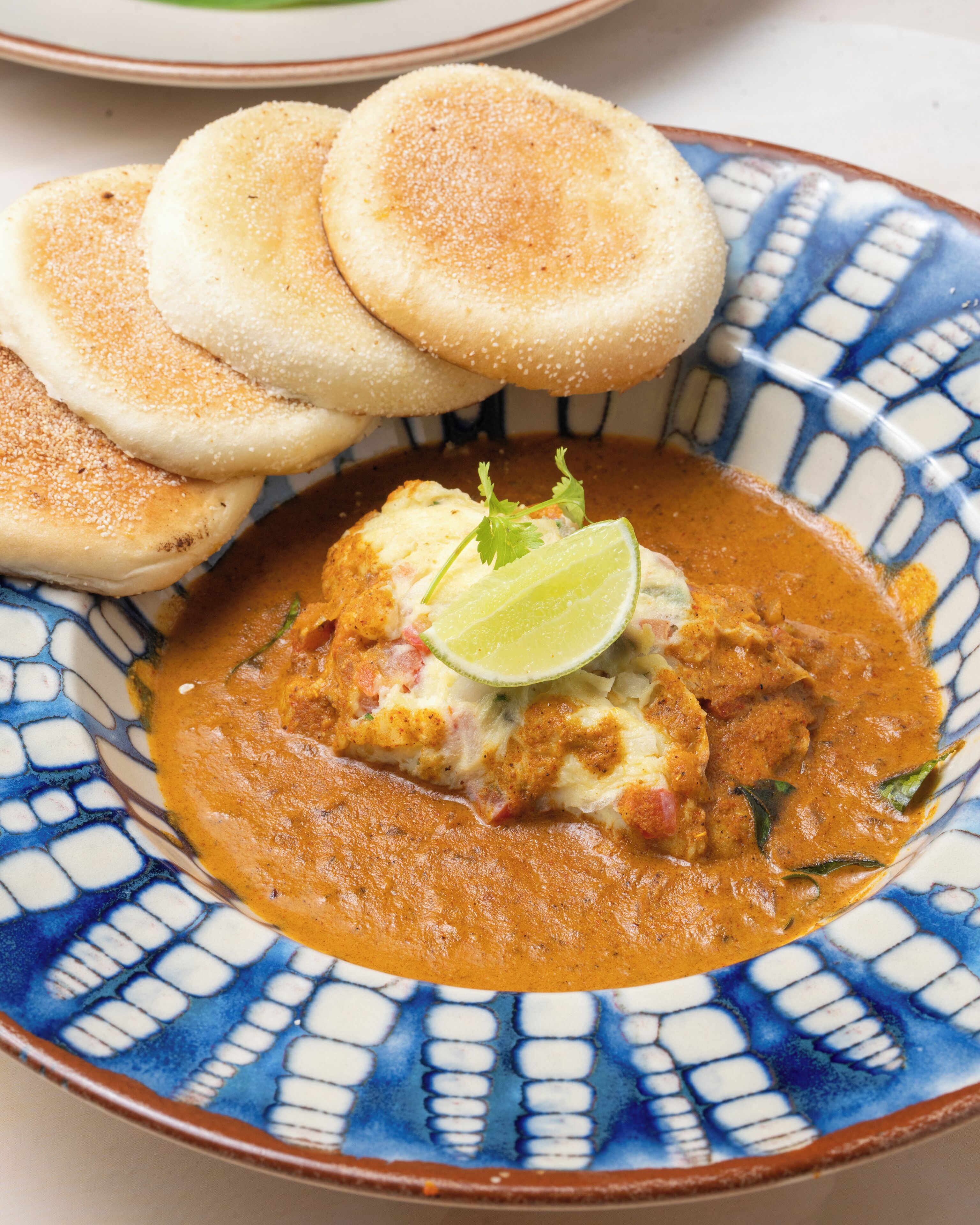 Eine Schüssel Curry mit Brot und einem Limettenschnitz.
