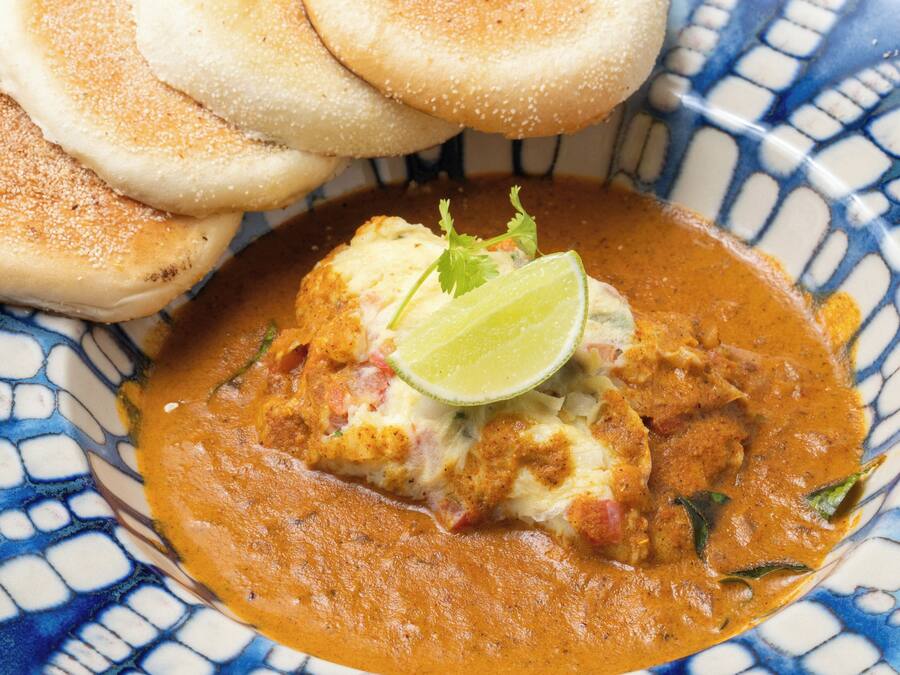 A bowl of curry with bread and a lime wedge.