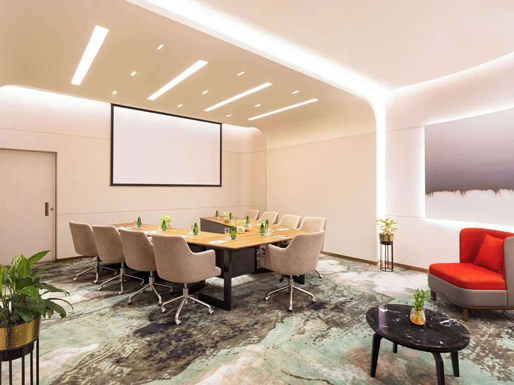 A conference room with a large table, chairs, a projector screen, and a carpeted floor.