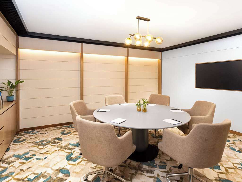 Un salón de conferencias con una mesa redonda, seis sillas y una lámpara de araña moderna.