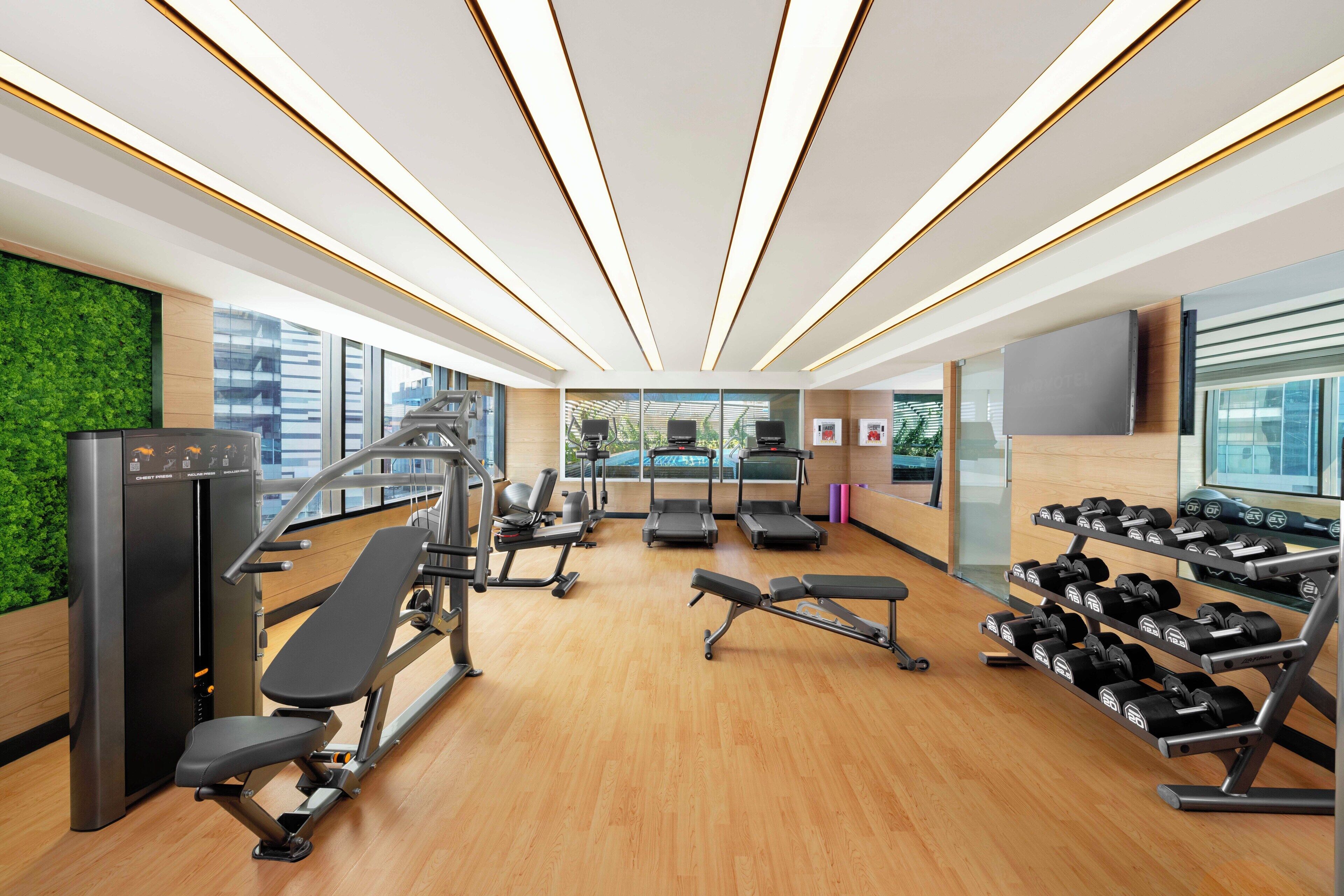 A modern gym with cardio machines, weight benches, and dumbbells.