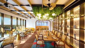 A spacious dining area with a long table, multiple chairs, and hanging plants. - Novotel GOA Panjim (Panaji)
