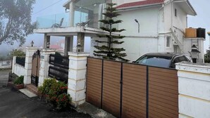 A two-story house with a balcony, a gated entrance, and a car parked in the driveway. - Sky Top Villa (Kodaikanal)