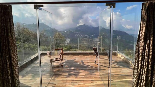 A balcony with a glass enclosure, wooden flooring, and a view of mountains and a waterfall. - Sky Top Villa (Kodaikanal)
