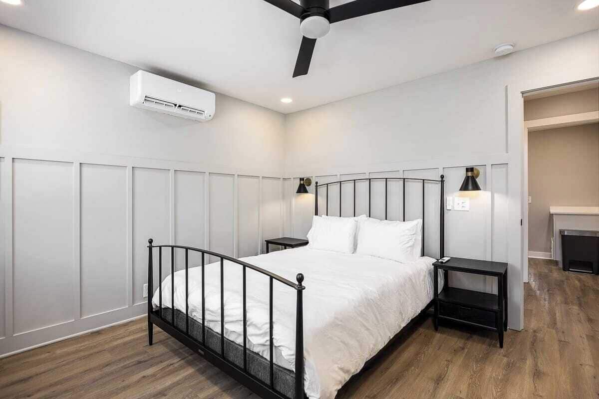 A bedroom with a metal bed frame, white bedding, two bedside tables, a ceiling fan, and an air conditioning unit.