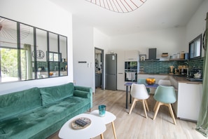 Un salon moderne avec un canapé vert, une petite table blanche et un coin repas composé de deux chaises.