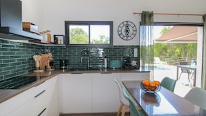 Een moderne keuken met een groene spatwand, witte kasten, een raam en een eethoek met een tafel en stoelen.