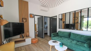 Een moderne woonkamer met een flatscreen televisie, een groene bank, een gele fauteuil, een klein witte tafeltje en een houten accentmuur.