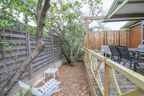 Une terrasse en bois avec des meubles d’extérieur, une petite table et un arbre.